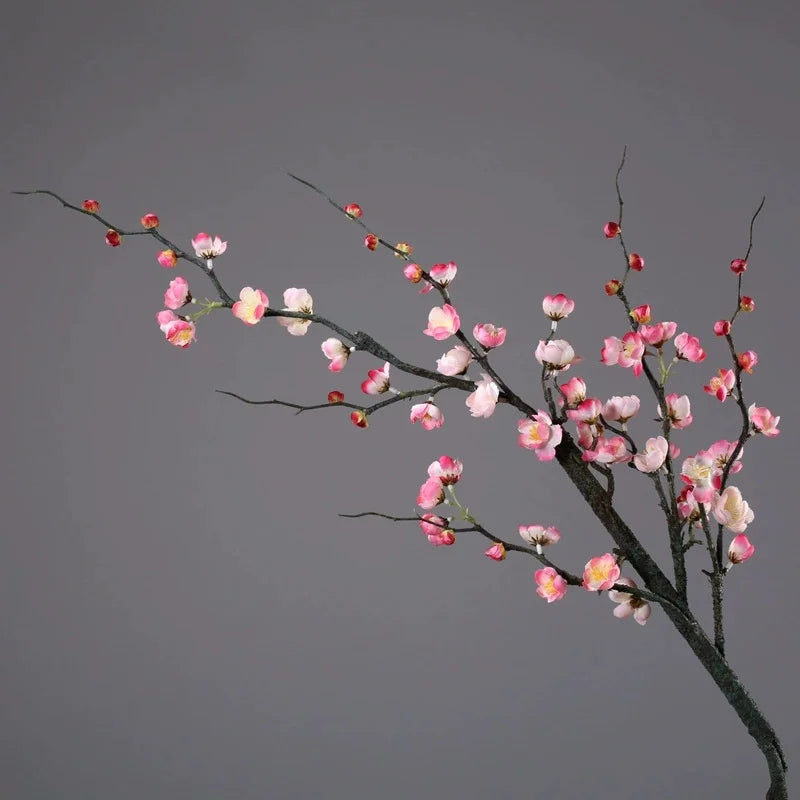 A delicate branch of artificial plum blossoms with pink and white flowers against a gray background.