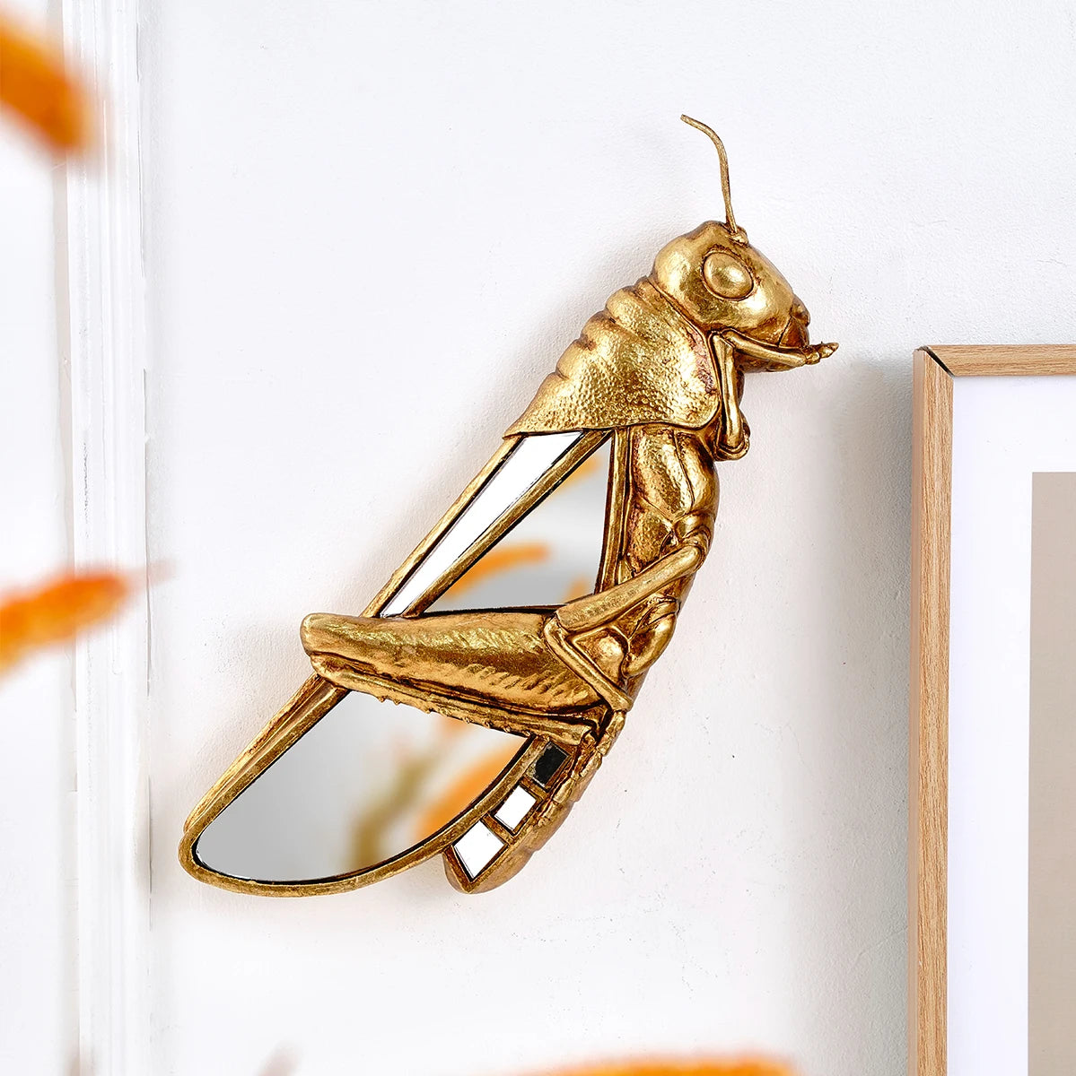A gold resin animal wall hanging decor shaped like a bird or insect, mounted on a white wall.