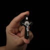 A hand holds a black wooden crucifix pendant depicting Jesus Christ on the cross.