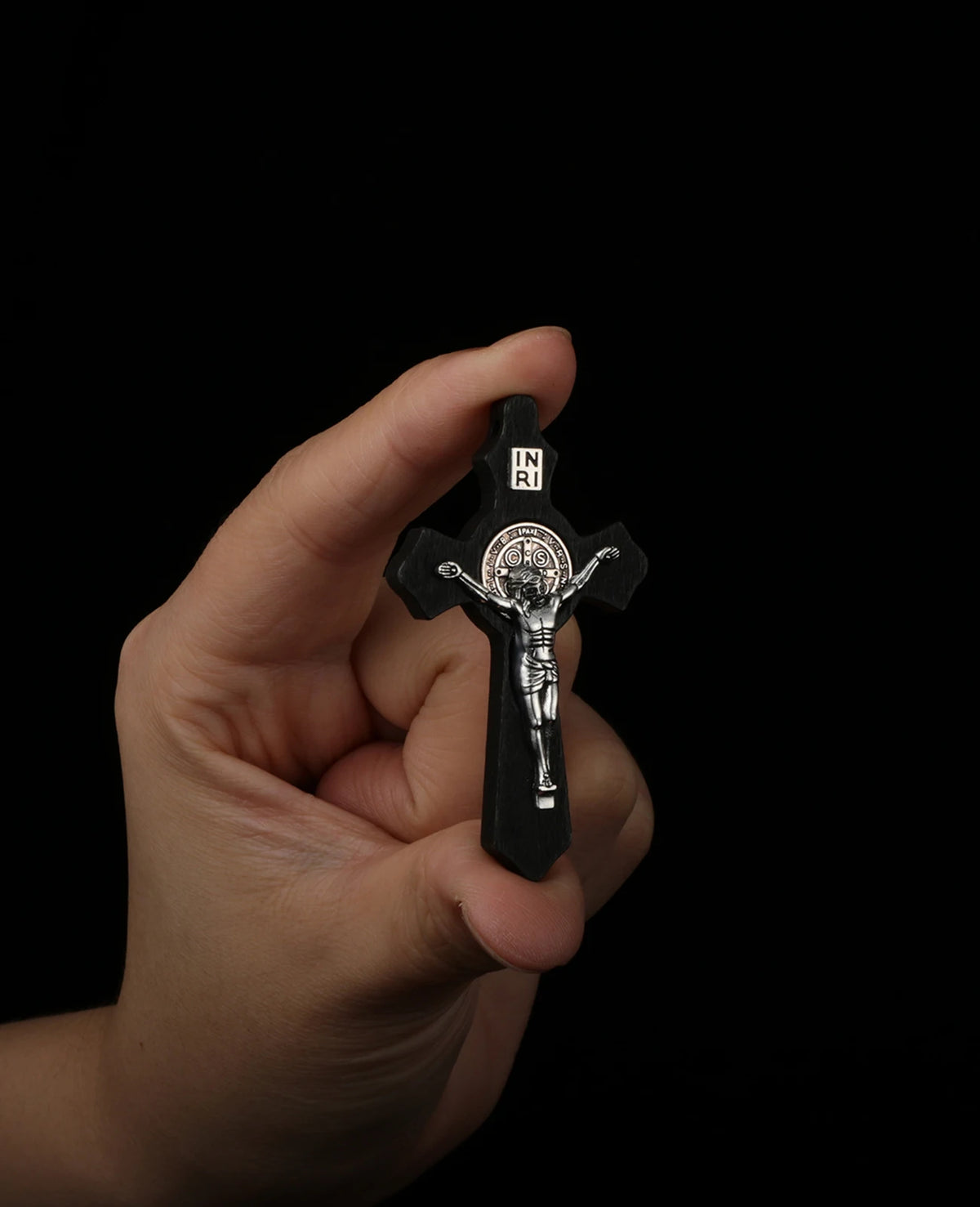A hand holds a black wooden crucifix pendant depicting Jesus Christ on the cross.