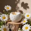 White textured silicone mold for candles, resin, and concrete resting on a wooden log surrounded by white daisies.