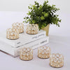 A set of gold-toned crystal tealight candle holders displayed on a white wooden surface next to a potted green plant.