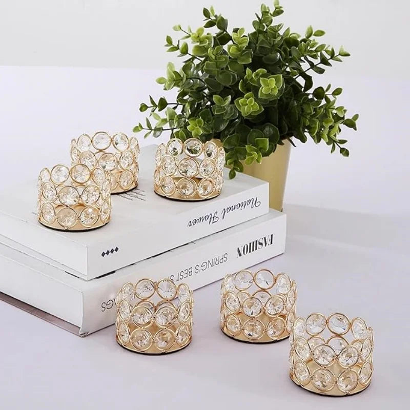 A set of gold-toned crystal tealight candle holders displayed on a white wooden surface next to a potted green plant.