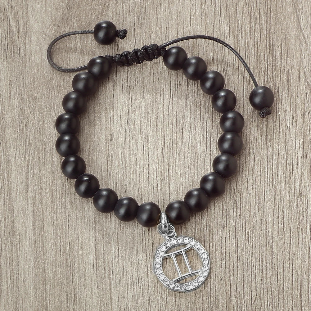A handmade beaded bracelet with natural black stones and a silver zodiac sign charm
