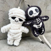 A plush keychain featuring a mummy and skeleton character in white and dark gray.