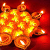 A close-up of numerous glowing orange marigold oil lamps arranged on a red surface.