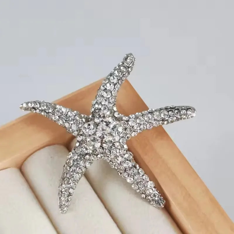 A silver vintage marine life brooch pin set shaped like a starfish resting on a light wooden surface.