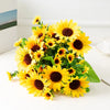A vibrant bouquet of artificial yellow sunflowers with dark brown centers and green leaves.