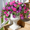 A white pedestal vase filled with vibrant pink and purple artificial petunia bundles on a wooden deck.
