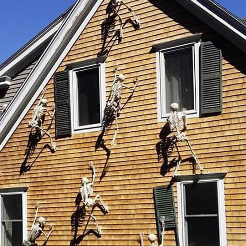 A close-up of a wooden house exterior showing several poseable human skeleton decorations mounted on the siding.