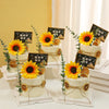 A display of yellow artificial sunflower heads arranged on white cake stands and decorated with greenery.