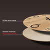 A close-up of a round wooden wall clock with a natural wood grain texture and black markings, shown next to a lighter colored