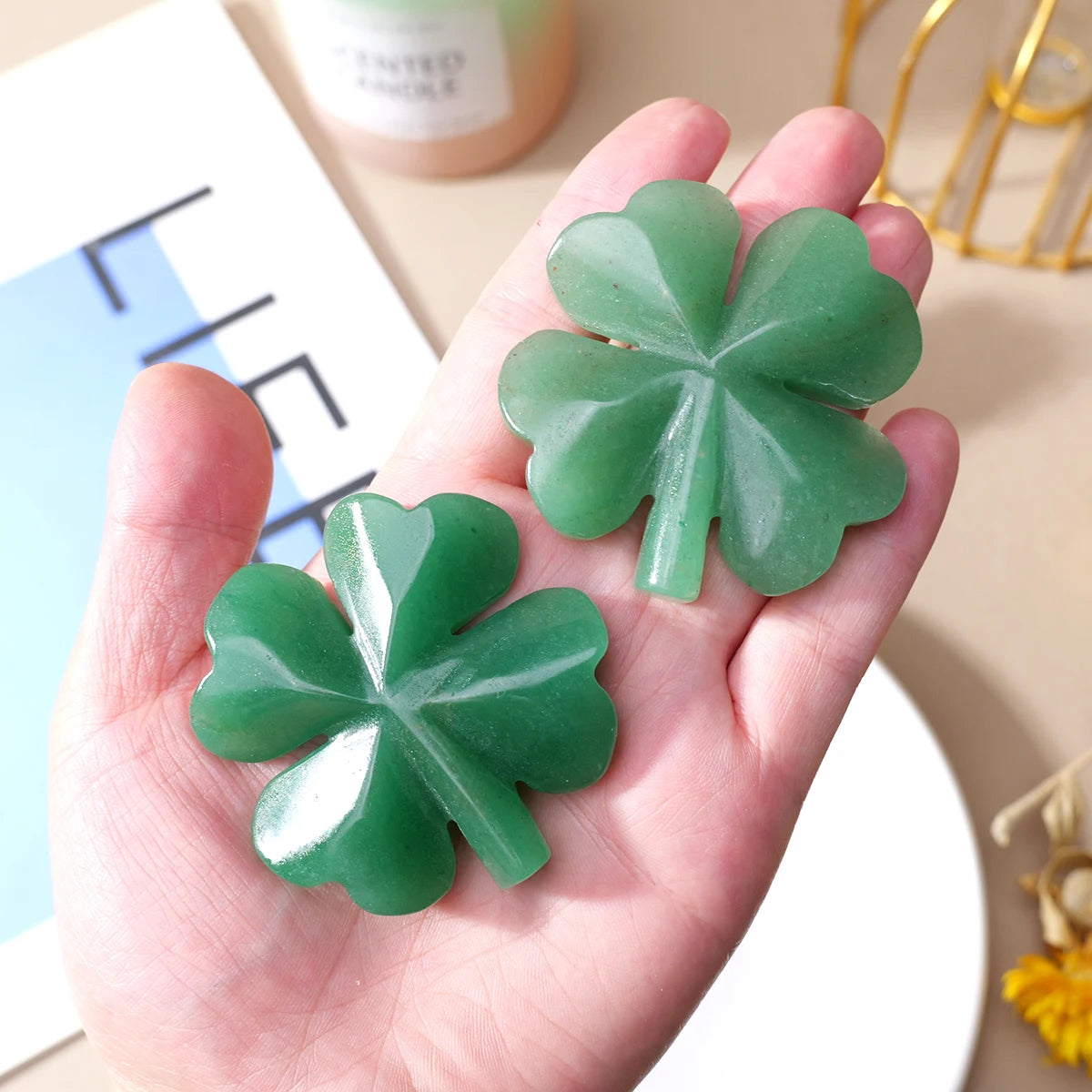 A hand holds a green natural aventurine quartz four-leaf clover crystal statue.