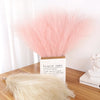 A bouquet of pink faux pampas grass reeds displayed in a cardboard box on a wooden surface.