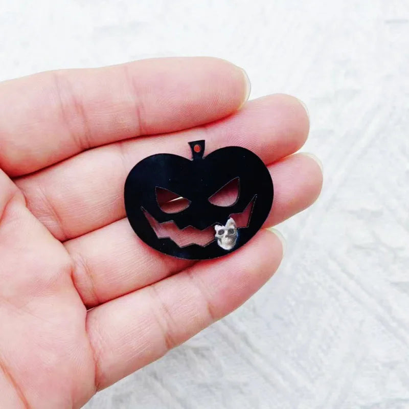 Una mano sostiene un colgante de acrílico negro de Halloween con la cara de una calabaza tallada y la silueta de un gato pequ