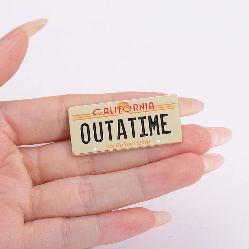 A gold-colored enamel pin shaped like a California license plate featuring the text OUTATIME The Golden State