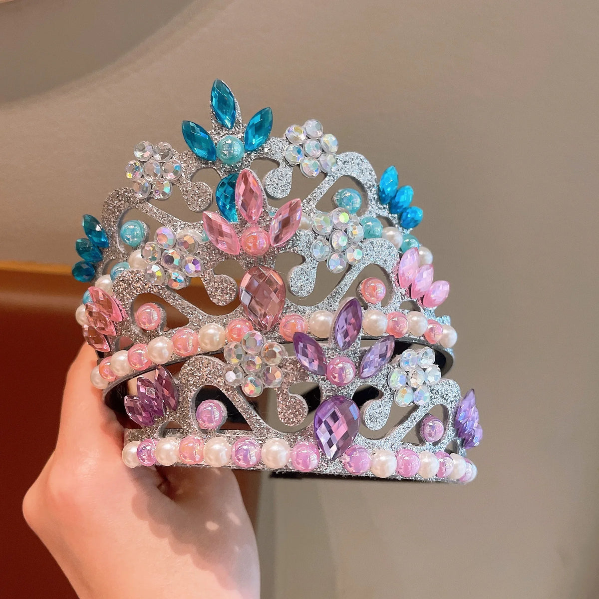 A silver crown adorned with pink, blue, and purple faux pearls and gemstones.