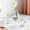 A set of three minimalist glass bud vases with a white flower arrangement on one, displayed on a white surface.