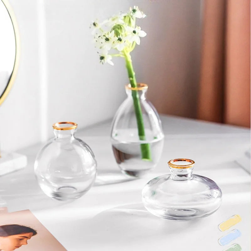 A set of three minimalist glass bud vases with a white flower arrangement on one, displayed on a white surface.
