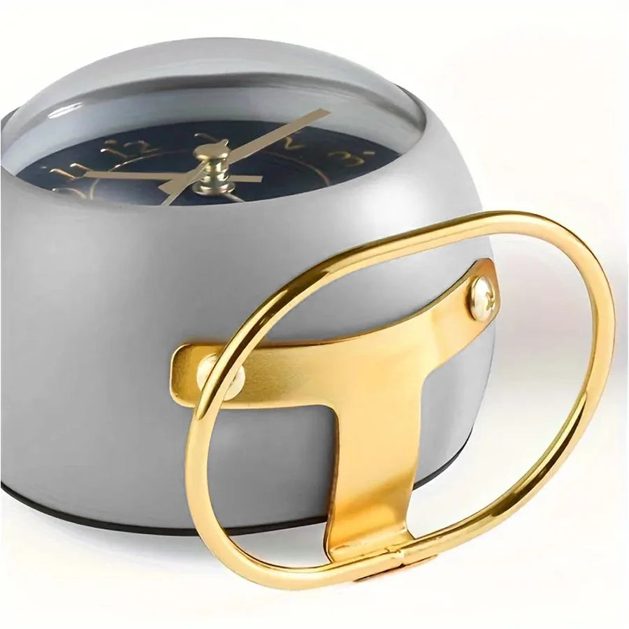 A minimalist Nordic alarm clock with a silver casing and gold accents, shown from the side.
