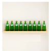 A row of green glass bottles of Nordic tea displayed on a natural wood floating shelf mounted on a white wall.