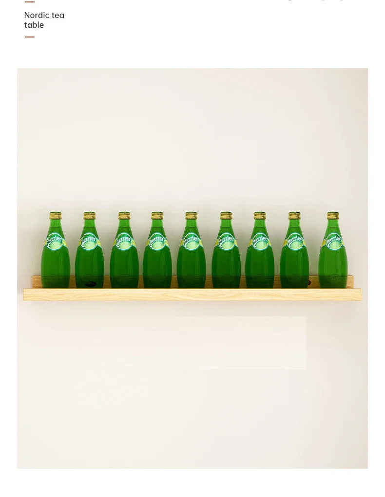 A row of green glass bottles of Nordic tea displayed on a natural wood floating shelf mounted on a white wall.