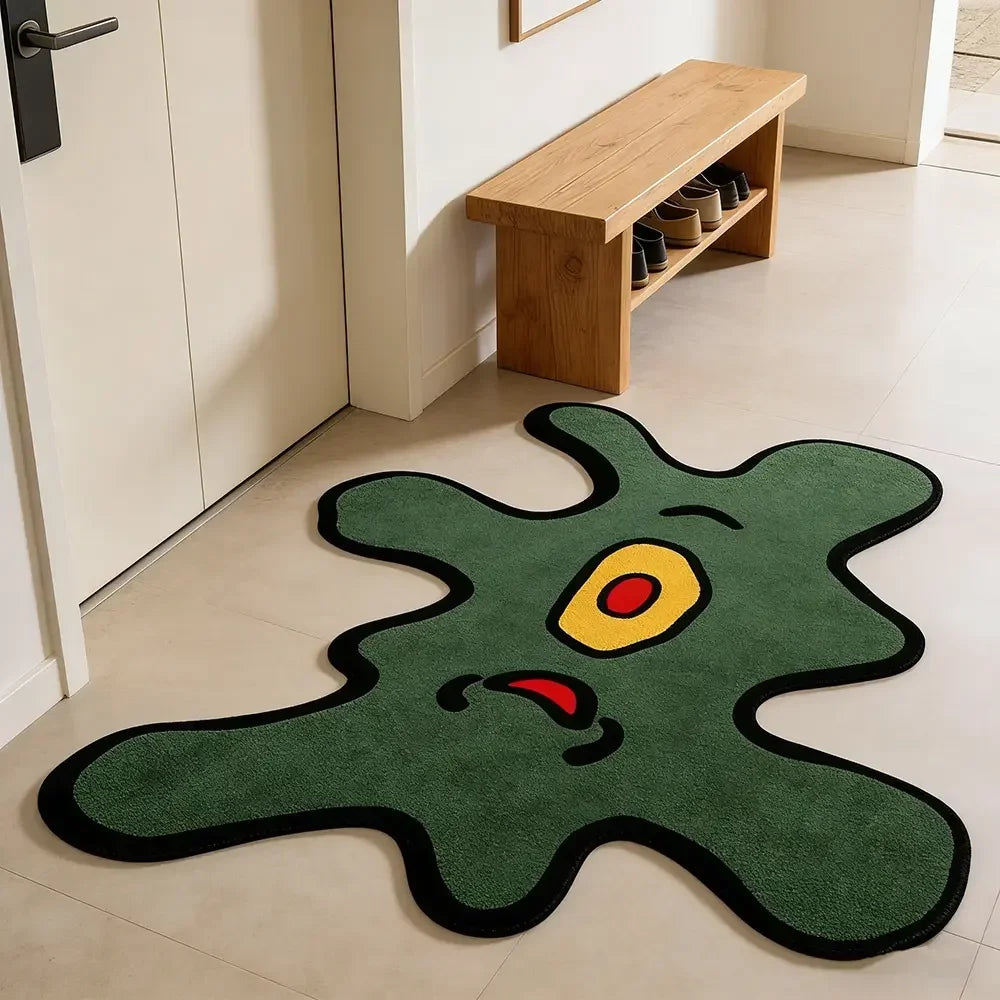 A green cartoon monster rug with yellow eyes and red mouth lying on a light floor.