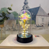 Une rose de verre éternelle avec une lumière LED est exposée sur une surface blanche devant un bâtiment d'église.