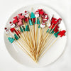 Red and green Christmas-themed cocktail picks with white pearl tips arranged on a white plate.
