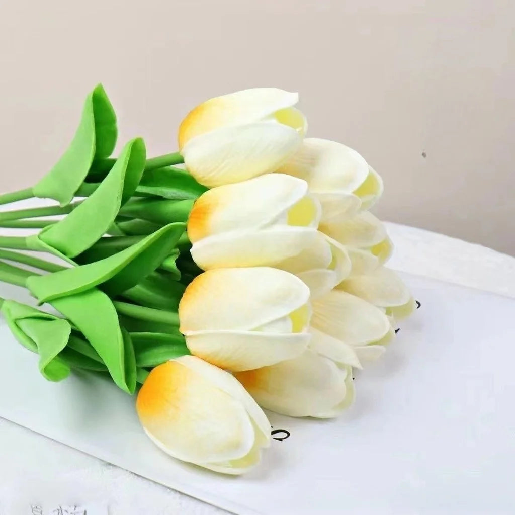 Un ramo de flores artificiales de tulipanes blancos y amarillos sobre una superficie blanca.