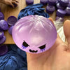 A hand holds a translucent purple silicone fidget dumpling with a spooky face design against a dark blue fabric background.
