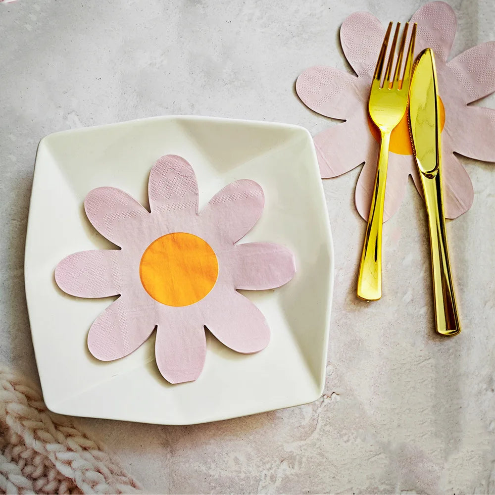 A white plate features a pink daisy flower cutout, accompanied by a gold fork and knife on a light gray surface.