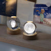 A crystal ball night light with a glowing moon inside rests on a wooden base next to a colorful illustration.