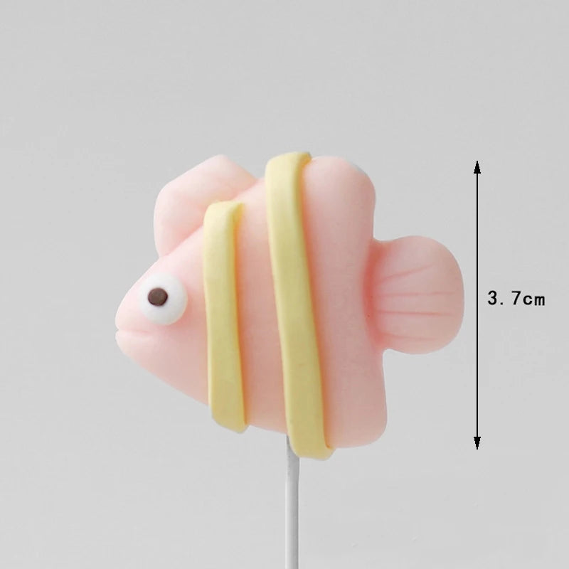 A pink cake topper featuring a crab, with a yellow striped element, shown against a light gray background.