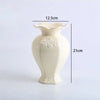 A cream-colored ceramic vase with a flared rim and floral relief detailing, shown from the side.