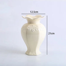 A cream-colored ceramic vase with a flared rim and floral relief detailing, shown from the side.