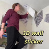 A person is demonstrating a 3D wall sticker featuring an impossible maze cube pattern on a white wall.