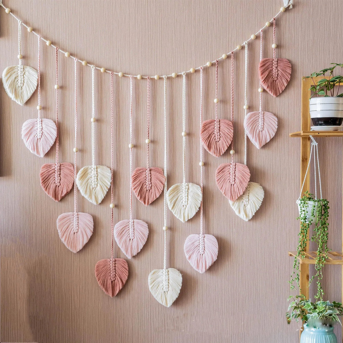 Bohemian macrame leaf wall hanging featuring pink and cream tassels suspended against a beige wall.