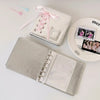 A silver leather photo album with a clear cover and pink ribbon accents is displayed next to small decorative pins.