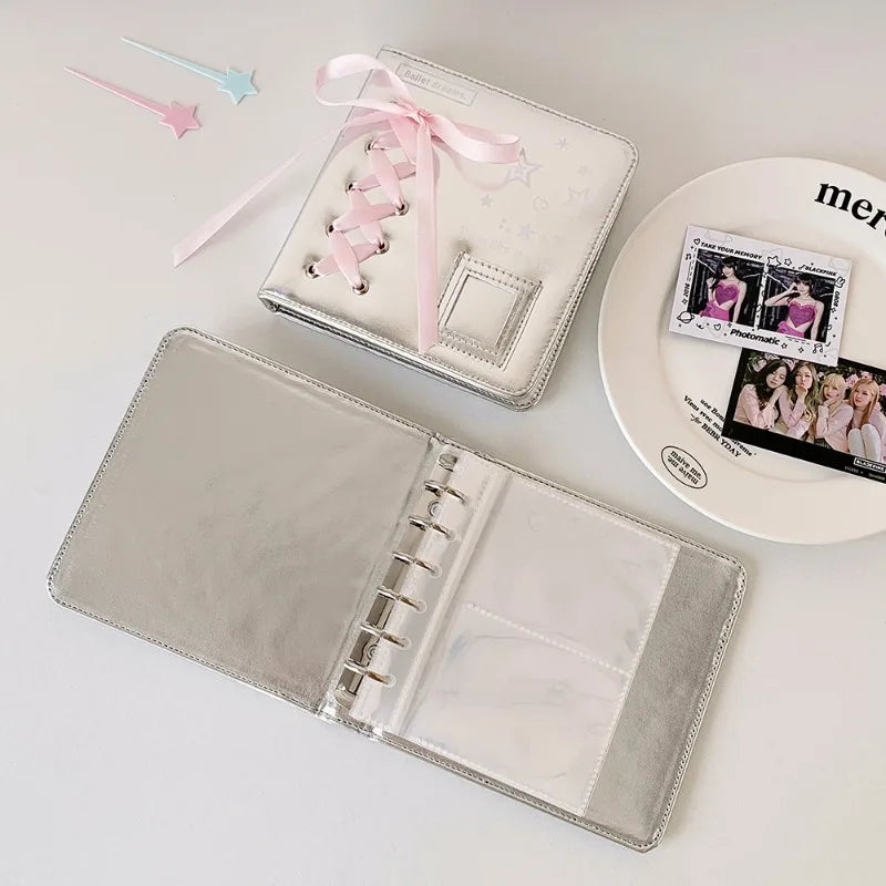 A silver leather photo album with a clear cover and pink ribbon accents is displayed next to small decorative pins.