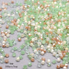 A pile of faceted bicone glass beads in mixed shades of green, pink, and amber for jewelry making.