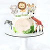 A white cake decorated with jungle animal toppers including a lion, elephant, giraffe, and zebra.