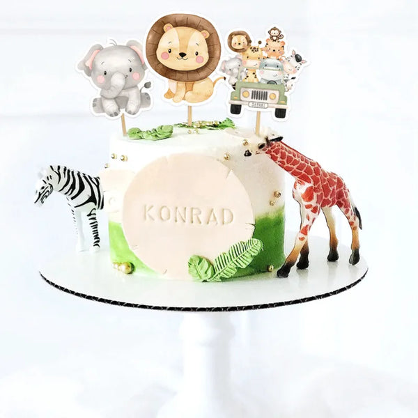 A white cake decorated with jungle animal toppers including a lion, elephant, giraffe, and zebra.
