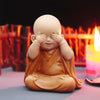 A small, tan resin figurine of a monk with hands covering his eyes in a meditative pose.