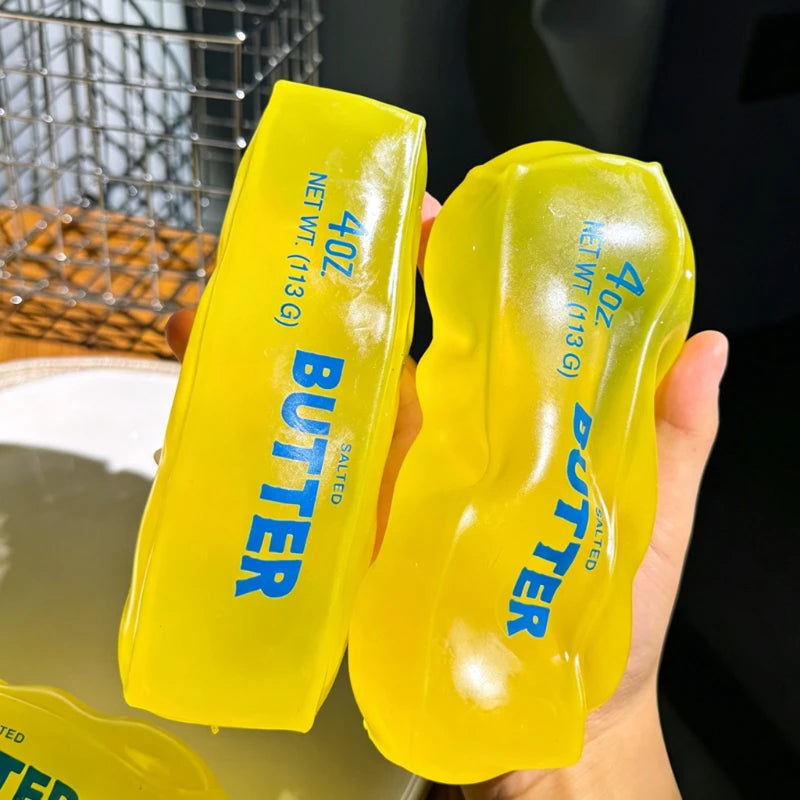 Une main tient un jouet anti-stress en forme de beurre jaune vif.