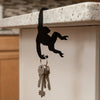 A black monkey-shaped storage hook with a banana design hanging on a white cabinet.