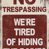 A vintage tin sign with a distressed texture displaying the text NO TRESPASSING WE'RE TIRED OF HIDING THE BODIES