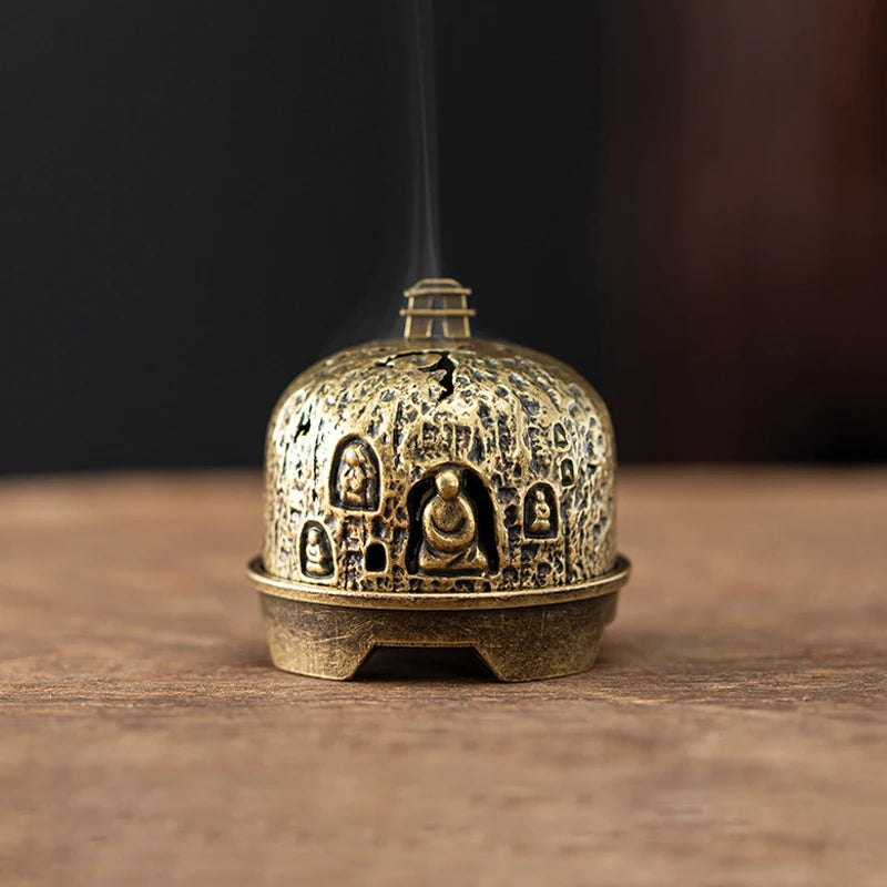 A vintage brass incense burner holder with a dome shape and small relief carvings sits on a wooden surface.