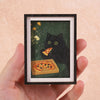 A framed print featuring a black cat and pizza design on a dark green background.
