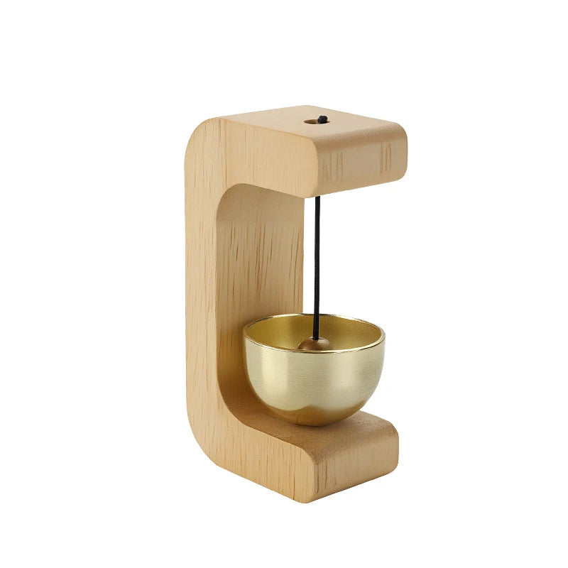 A wooden doorbell featuring a brass chime suspended by a string, mounted on a light wood frame.